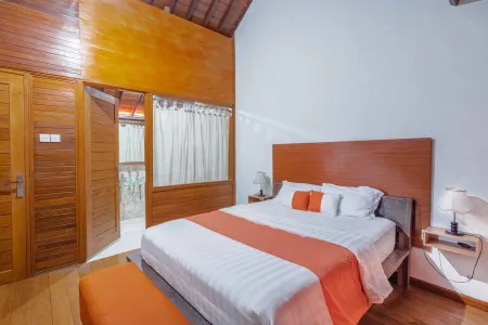Cozy Balinese-style bedroom with king-size bed, orange wood accents, white linens, and open balcony doors.